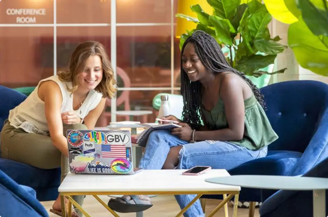 Two women sitting, laughing, and looking at a laptop
